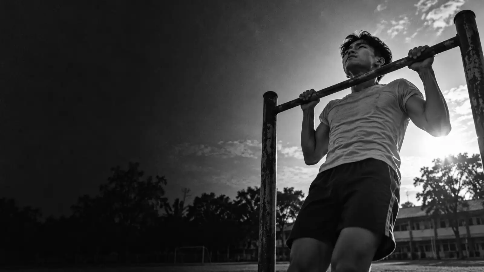 Foto hitam putih remaja melakukan pull-up di lapangan sekolah
