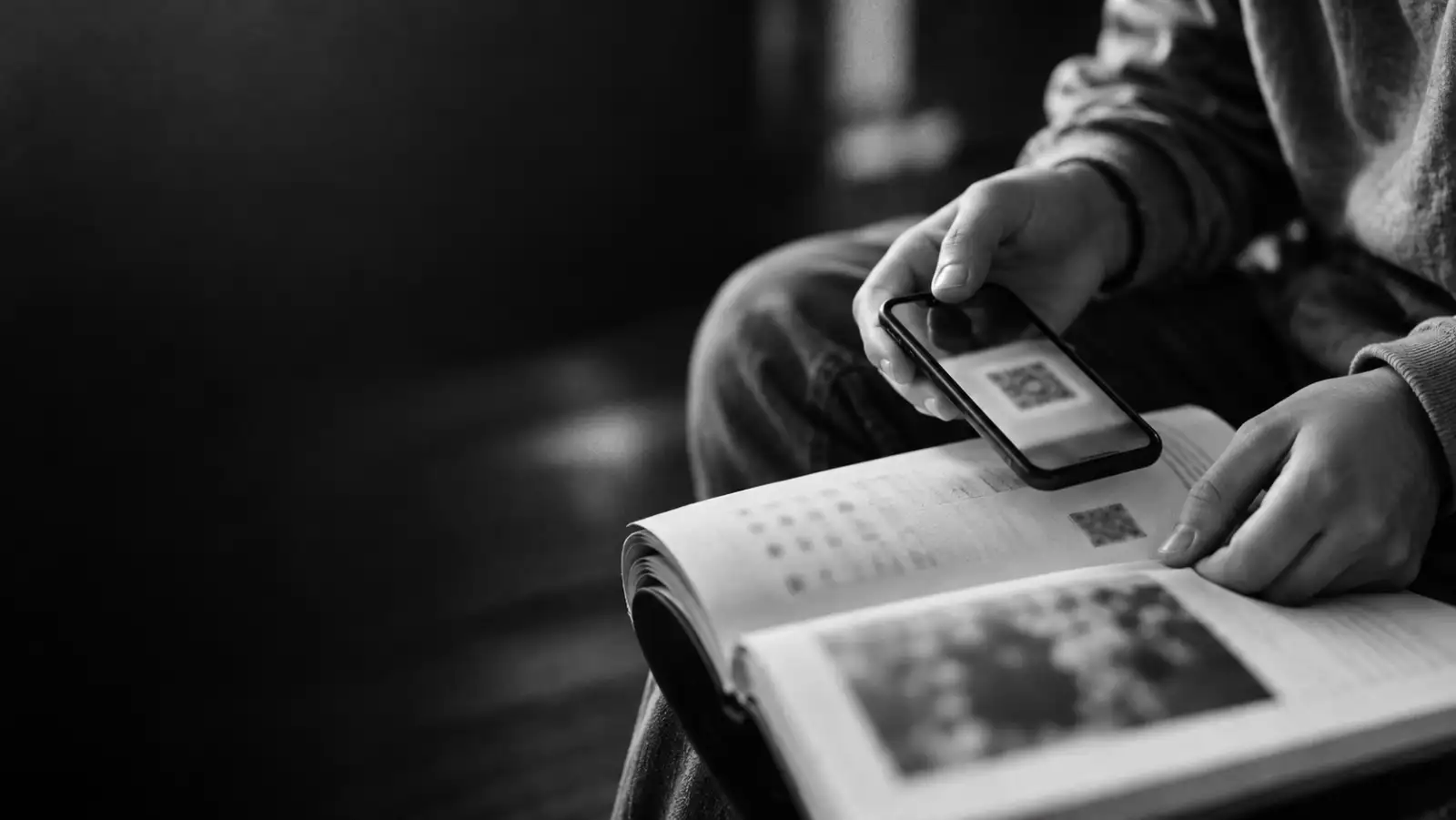 Foto hitam putih tangan remaja memindai kode di halaman buku dengan ponsel